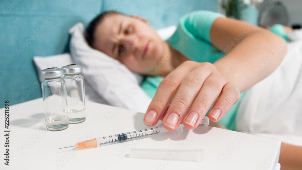 Closeup photo of young sick woman taking syringe with painkiller medicine from bedside table Closeup photo of young sick woman taking syringe with painkiller medicine from bedside table