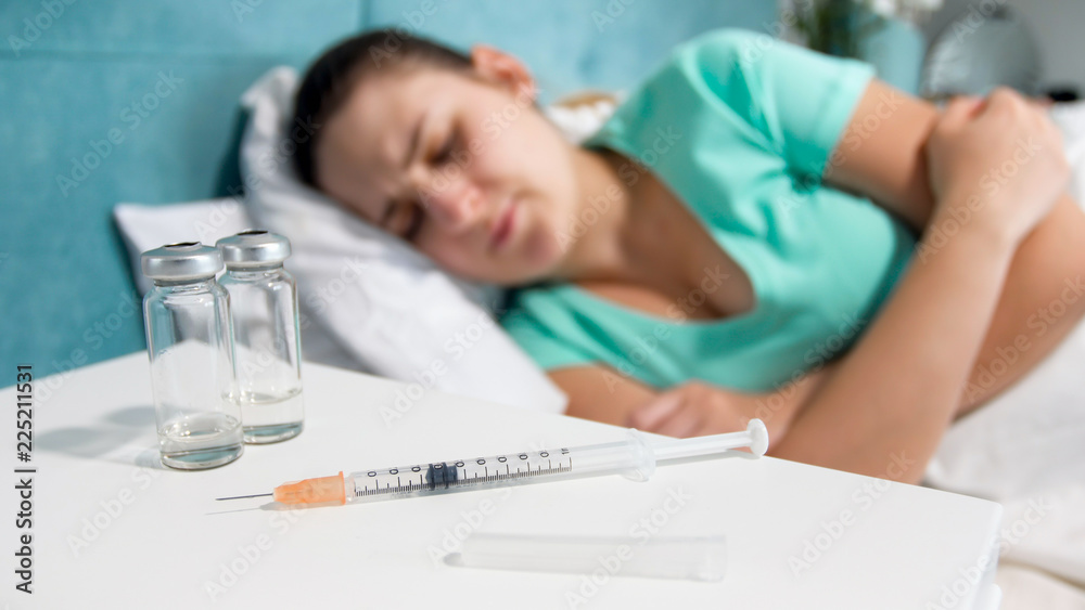 Closeup image of syringe with medicines and sick woman lying in bed
