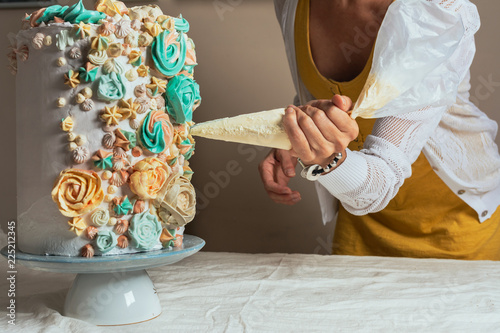 Woman pastry chef decorating a cake with a pastry bag with cream photo