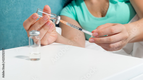 Closeup image of young woman lying in bed and preparing syringe for injection
