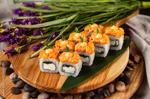 Lava maki sushi rolls with cream cheese at wooden tray decorated with lavender flowers and stones background.