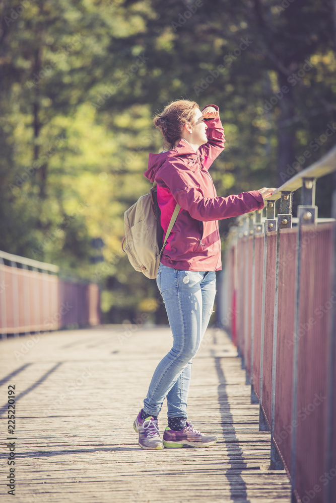 Junge Frau auf Brücke blickt der Sonne entgegen, Herbsttag