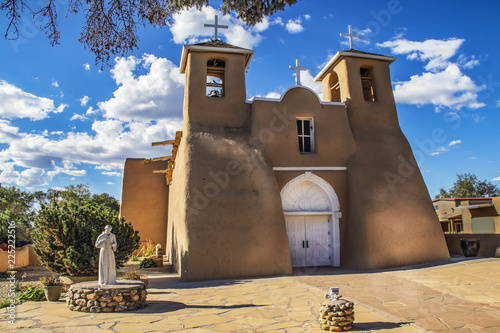 Historic adobe San Francisco de Asis Mission Church in Taos New Mexico in dramatic late afternoon light under intense blue sky with fluffy while clouds and birds in the belfry photo