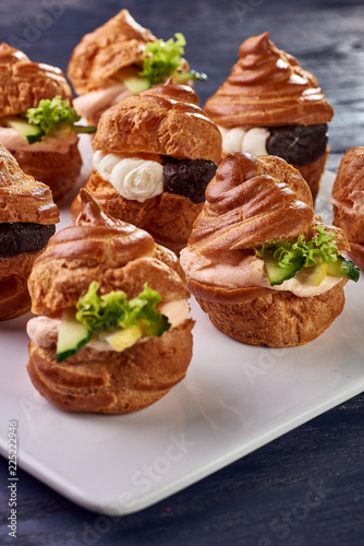 Savory profiteroles with different types of fillings. Salty cakes for snacks. Mini sandwiches, canapes with vegetables, meat, liver, sauce. An exquisite French snack for a buffet at the feast.