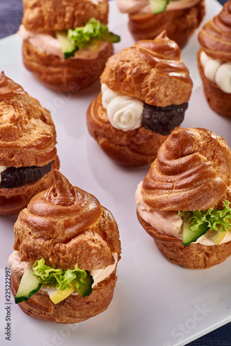 Savory profiteroles with different types of fillings. Salty cakes for snacks. Mini sandwiches, canapes with vegetables, meat, liver, sauce. An exquisite French snack for a buffet at the feast.