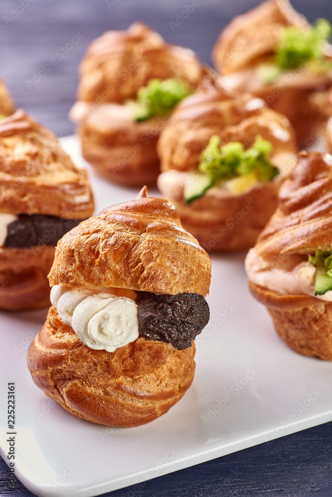 Savory profiteroles with different types of fillings. Salty cakes for snacks. Mini sandwiches, canapes with vegetables, meat, liver, sauce. An exquisite French snack for a buffet at the feast.