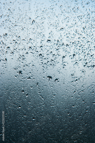 The texture of large raindrops on the glass is a beautiful background in neutral cool blue and dark colors of water – vertical photo of the window
