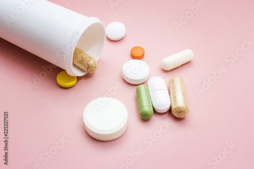 Tablets and pills from a bottle on a pink background