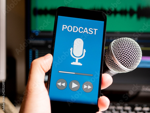 Podcast stuido. Phone with podcast app playing in front of microphone and edting program on screen.