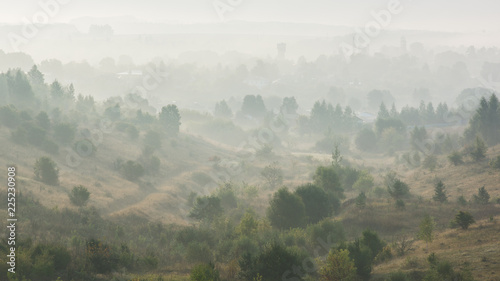 Summer morning landscape. Green hills with trees in dence mist at dawn before sunrise
