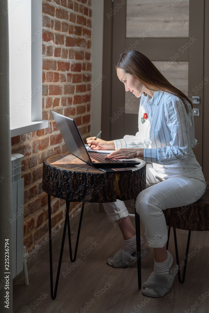 Vertical portrait of a brunette working on a laptop in the room. Vertical portrait of a brunette working on a laptop in the room.
