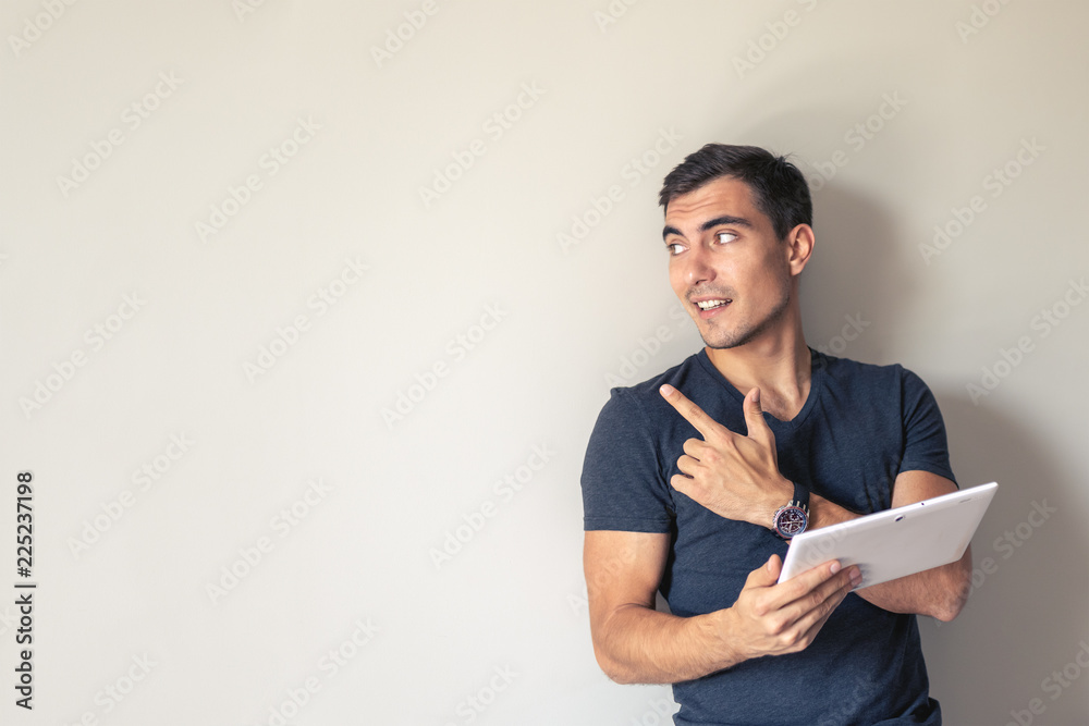 Man for conceptual design. A handsome young man uses a tablet standing at a gray wall, copy space Man for conceptual design. A handsome young man uses a tablet standing at a gray wall, copy space