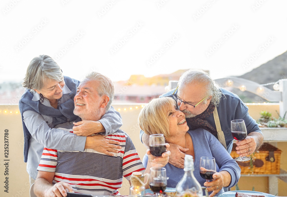 Happy senior friends having fun  drinking red wine in terrace outdoor - Older people enjoying dinner and laughing together - Friendship and elderly lifestyle concept