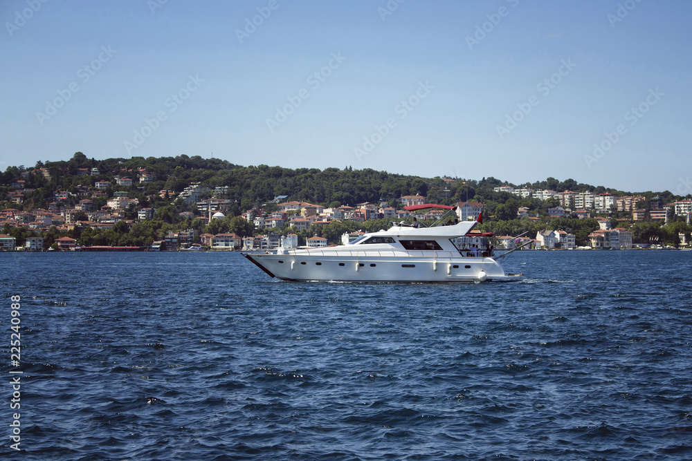 Unrecognizable people ride luxury white yacht on Bosphorus in a sunny summer day in Istanbul. European side is in the background.