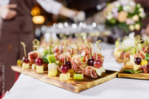 The waiter prepared and serves a snack. the buffet at the reception. Assortment of canapes on wooden board. Banquet service. catering food  snacks with cheese  jamon  prosciutto and fruit