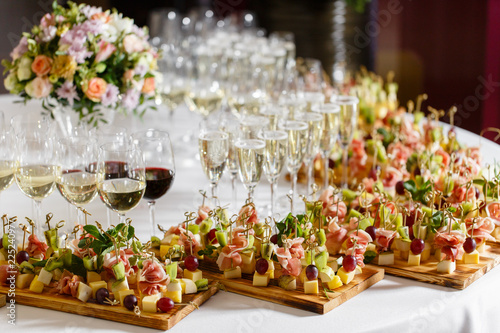the buffet at the reception. Glasses of wine and champagne. Assortment of canapes on wooden board. Banquet service. catering food, snacks with cheese, jamon, prosciutto and fruit