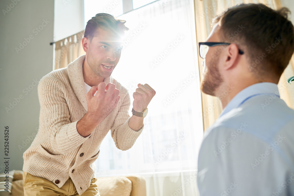 Obraz premium Portrait of emotional man clenching fists during therapy session with psychiatrist , copy space