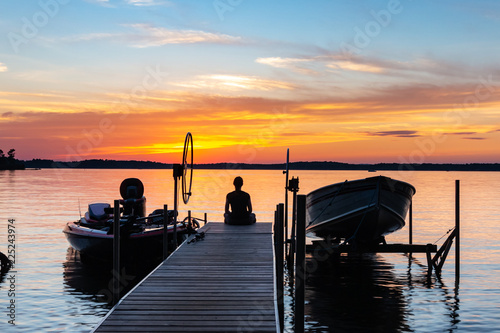 Young woman sitting on the end of a pier, watching the colorful sunrise. Vacation, travel, relaxation concepts