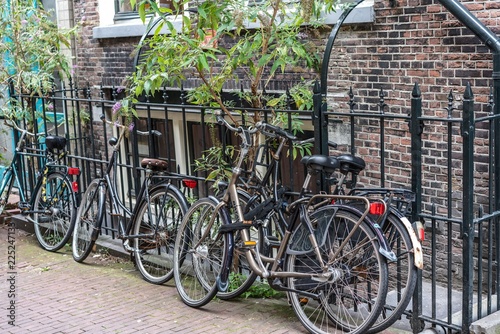 Alte Fahrräder angelehnt an geschmiedeten Eisenzaun, dahinter eine backsteinziegel Häuserfront 
