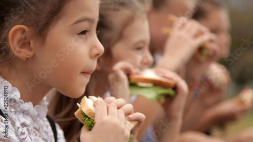 Children in school uniform after classes spend time in the park at the bottom of a sandwich. Delicious food, a sandwich day