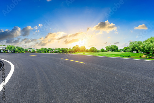 Empty asphalt road and green forest with colorful clouds at sunset