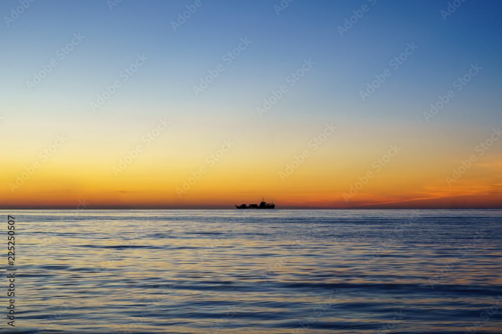 Silhouette of sailing ship far away at the sea horizon during sunset. With text copy space.
