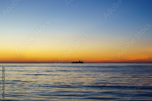 Silhouette of sailing ship far away at the sea horizon during sunset. With text copy space.