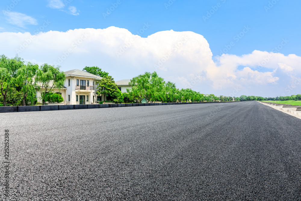 Fototapeta Empty asphalt road and forest with apartment buildings in the city suburbs