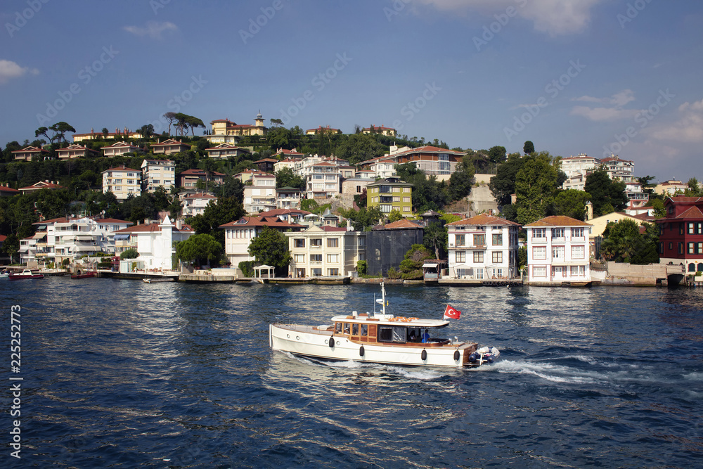 View of a small wooden fishing boat on Bosphorus. Historical, old Turkish / Ottoman houses on Asian side of Istanbul are in the background. It is a sunny summer day.