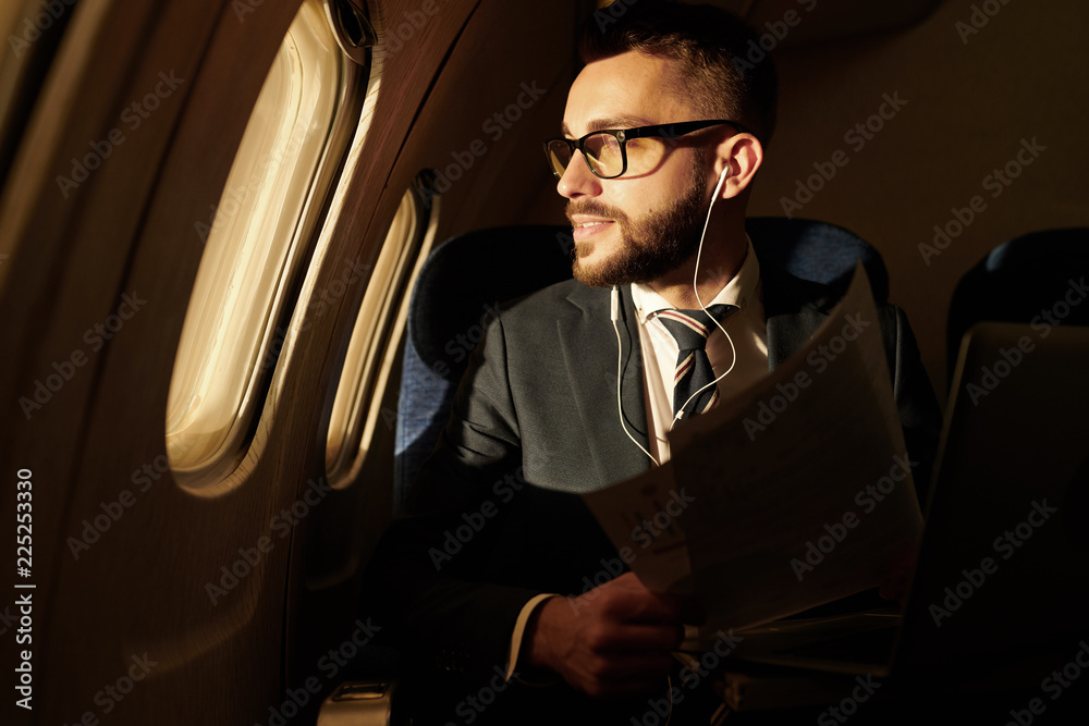 Naklejka premium Side view portrait of smiling young businessman looking in window enjoying sunset view from plane, copy space