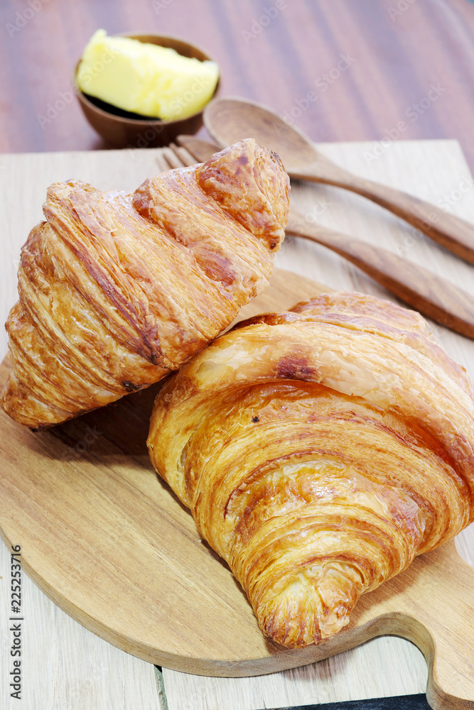 Croissant with butter on a wooden background.