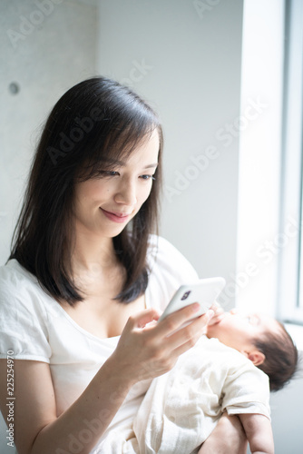 赤ちゃんを抱きながらスマートフォンを使う女性