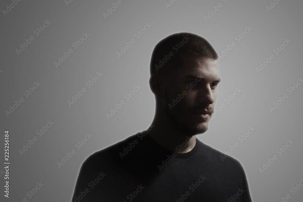 one young man, 20-25 years, moody dark portrait, side view. studio shot, gray background. head and shoulders shot.