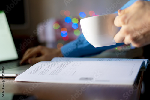 close up student doing homework on the table at home, using naptop and book, drink tea f