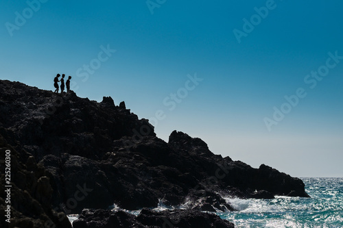 3 teenage boys on cliff at an ocean beach on the big island of Hawaii HI United States