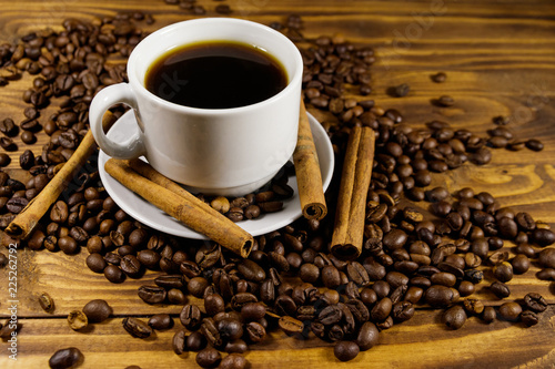 Cup of coffee, roasted coffee beans and cinnamon sticks on wooden table