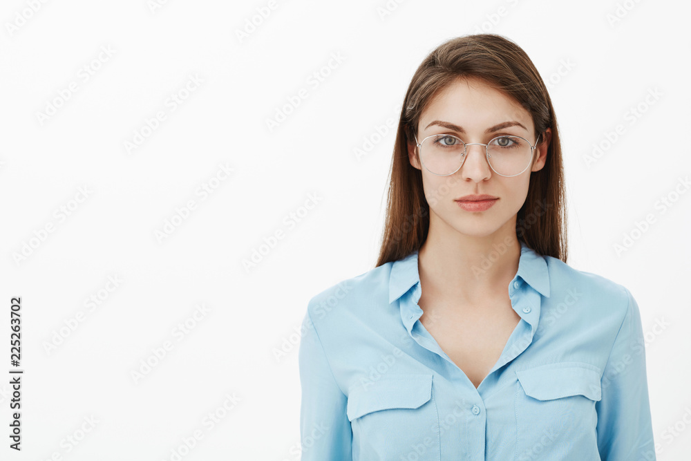 Waist-up shot of confident smart good-looking woman with brown hair in trendy glasses and blue blouse staring at camera with self-assured expression, standing over grey wall ready for work and action Waist-up shot of confident smart good-looking woman with brown hair in trendy glasses and blue blouse staring at camera with self-assured expression, standing over grey wall ready for work and action