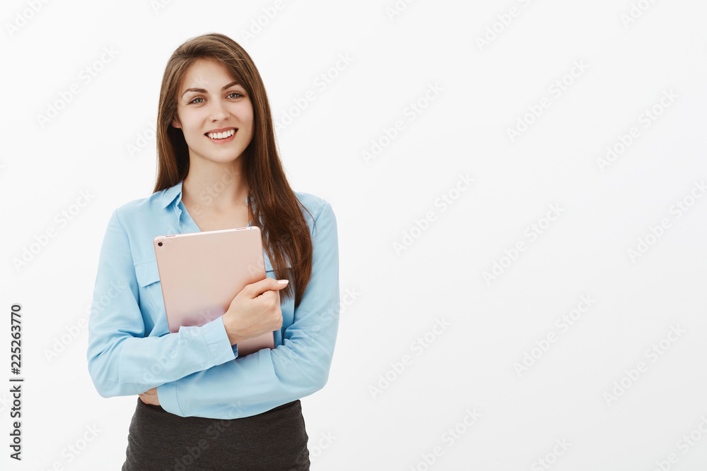 Positive attractive woman in office blouse, holding digital tablet with crossed hands on chest, smiling broadly, being friendly and polite, staring working at new place, meeting coworkers Positive attractive woman in office blouse, holding digital tablet with crossed hands on chest, smiling broadly, being friendly and polite, staring working at new place, meeting coworkers