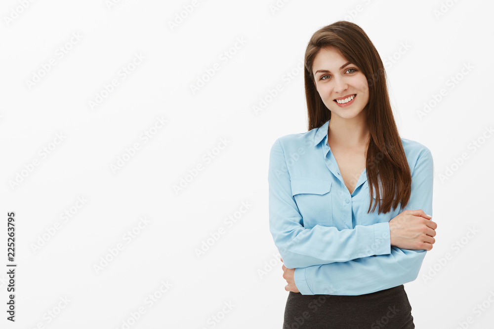Studio shot of good-looking polite female coworker in official blue blouse, hugging herself with hands crossed on chest, gazing with beautiful smile at camera, feeling nervous before important deal Studio shot of good-looking polite female coworker in official blue blouse, hugging herself with hands crossed on chest, gazing with beautiful smile at camera, feeling nervous before important deal