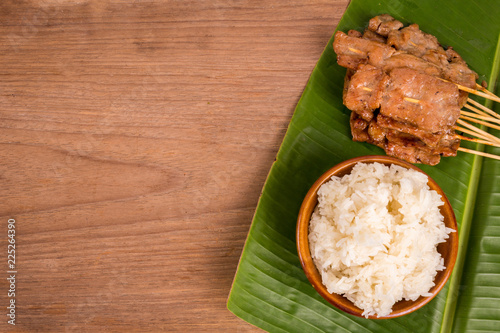 grilled pork or moo ping in Thai with sticky rice and Nam Prik Num (Northern Thai Green Chilli Dip) local street food on banana green leaf photo