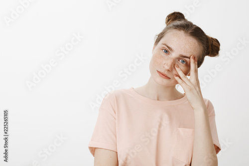 Girl trying listen carefully what friend talking about. Portrait of calm feminine girlfriend with freckels and blue eyes, holding hands on half of face, peeking through fingers and smirking at camera photo