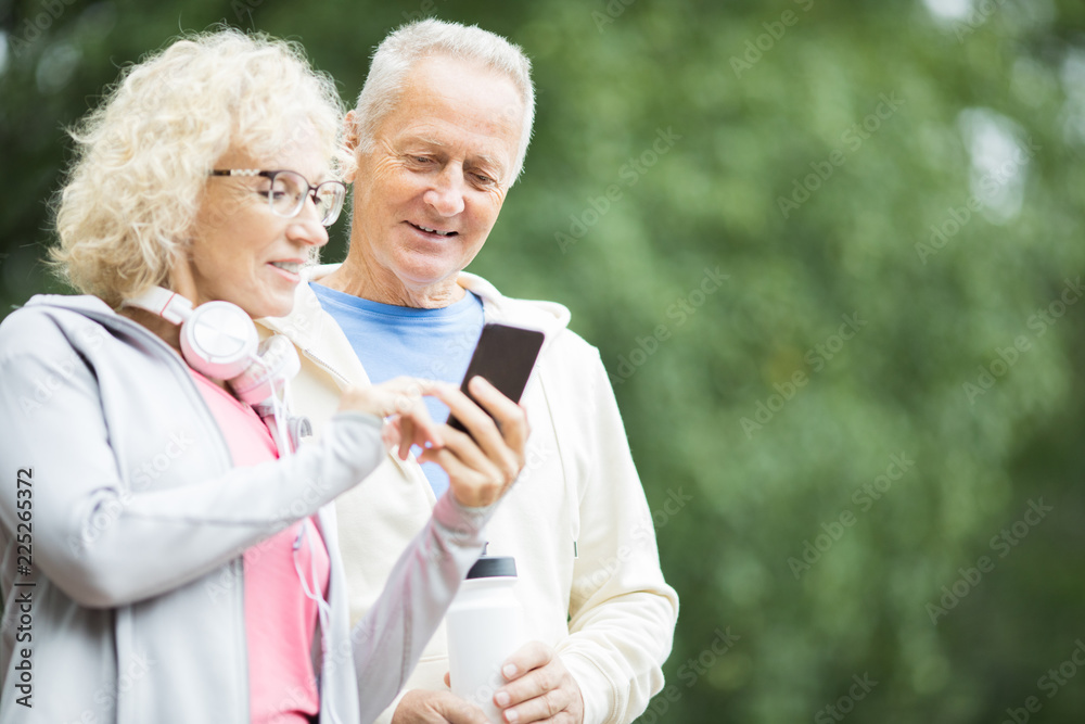 Aged female showing her husband something in smartphone after outdoor workout Aged female showing her husband something in smartphone after outdoor workout