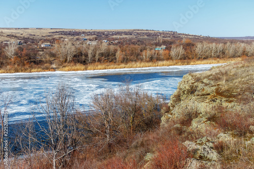 The rock above the winter frozen river with the village on the other side
