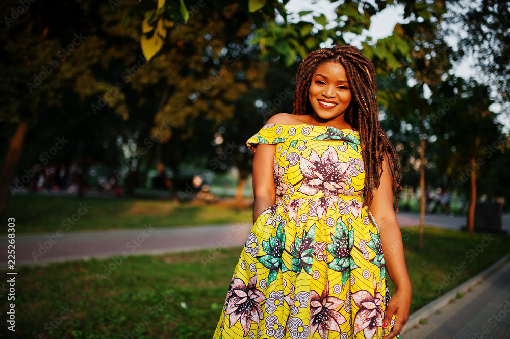Cute small height african american girl with dreadlocks, wear at coloured yellow dress, posed at sunset.