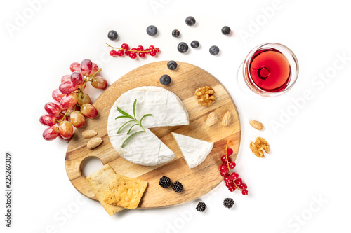 An overhead photo of Camembert cheese with a glass of red wine, fruits and nuts, shot from above on a white background with copy space
