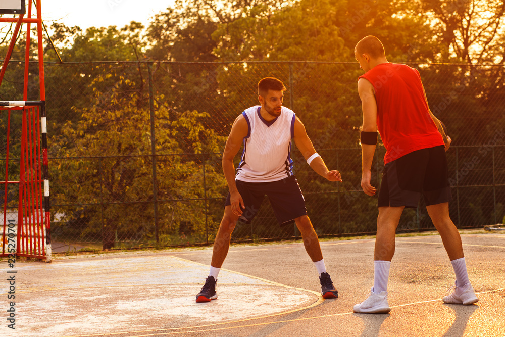 Two young friends playing basketball on court outdoors at sunset.