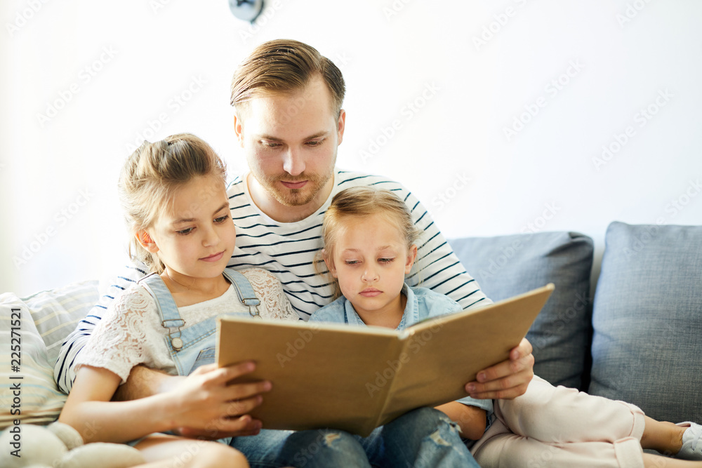 Young father and his two little daughters reading book of stories while staying at home Young father and his two little daughters reading book of stories while staying at home