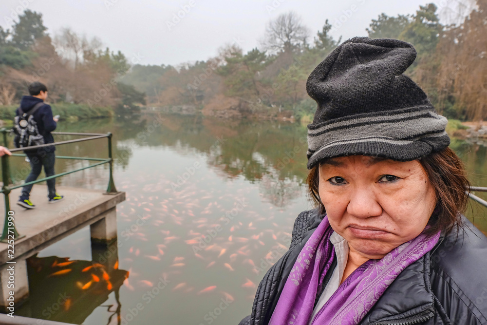 Happy old asian women traveler make a funny face in the xihu lake(west lake) park in hangzhou china Happy old asian women traveler make a funny face in the xihu lake(west lake) park in hangzhou china