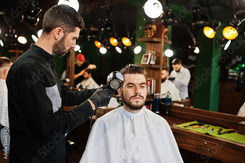 Handsome bearded man at the barbershop, barber at work, using hair dryer.