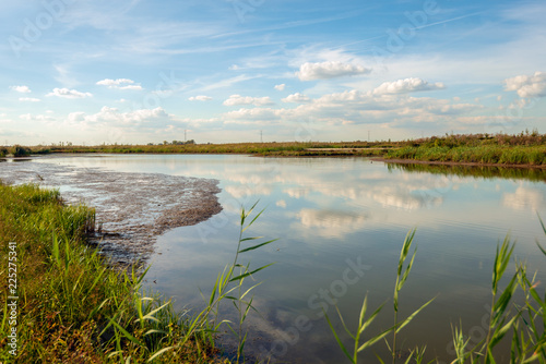 White clouds and a blue sky reflecting in the mirror smooth water surface of a wide creek